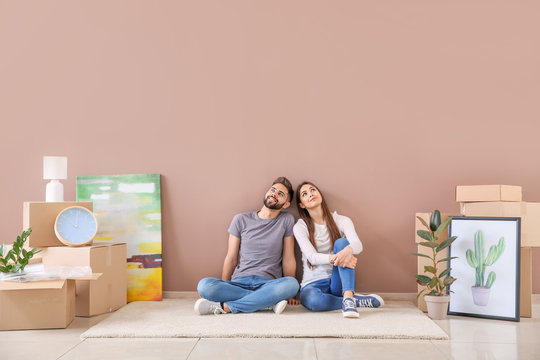 Young couple with belongings sitting near color wall in their new house