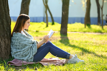 Beautiful young woman reading book in park