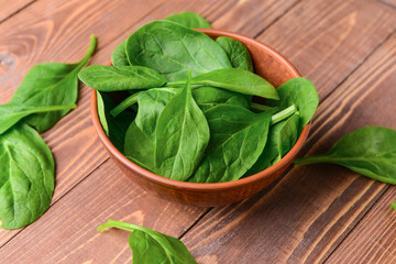 Bowl with fresh spinach on wooden background