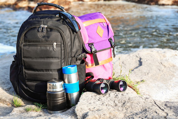 Tourist's backpacks with thermoses and binocular on rock near mountain stream