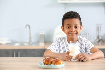 Cute African-American boy with glass of milk and buns at table