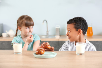 Cute children with glasses of milk and buns at table