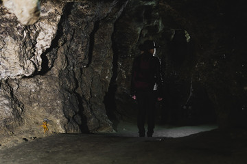 Obraz premium Silhouette Girl exploring huge cave. Adventure traveller dressed cowboy hat and backpack, leather jacket. extreme vacation, tourist route. ancient crystal formations, geology, village Kryvche. Ukraine
