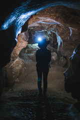 Silhouette Girl exploring huge cave. Adventure traveller dressed cowboy hat and backpack, leather...