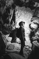 Obraz premium Girl exploring huge cave. Adventure traveller dressed cowboy hat and backpack, leather jacket. black and white, tourist route. ancient crystal formations, vertical photo, village Kryvche. Ukraine