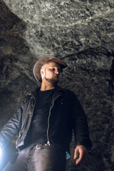Man exploring huge cave. Adventure travellers dressed cowboy hat and backpack, leather jacket....