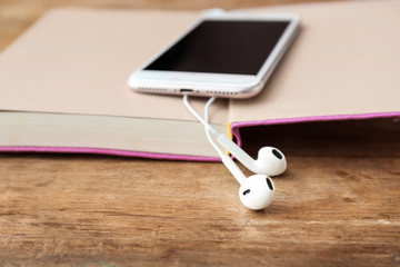 Book, mobile phone and modern earphones on wooden background, closeup. Concept of audiobook