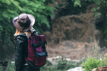 Young european female tourist with backpack and cowboy hat looking at the river washed away the bridge, the crossing was impossible. Deep waterfall. Copy space. adventure concept. active lifestyle