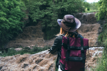 Young european female tourist with backpack and cowboy hat looking at the river washed away the bridge, the crossing was impossible. Deep waterfall. Copy space. adventure concept. active lifestyle