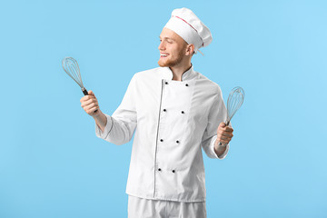 Handsome male chef with whisks on color background