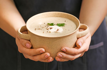 Woman holding pot of tasty mushroom cream soup, closeup