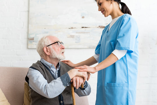 Side View Of Elderly Man And Nurse Standing In Room, Looking At Each Other