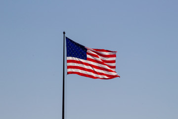 USA American flag waving in the wind on clear blue sky in background