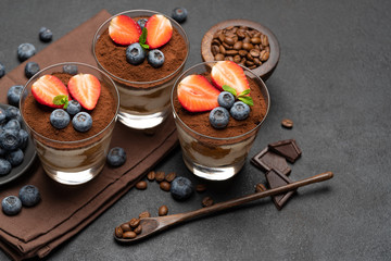 Classic tiramisu dessert with blueberries and strawberries in a glass on dark concrete background