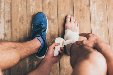 cropped view of sportsman in one sneaker bandaging injured leg with elastic bandage