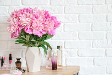 Vase with beautiful peony flowers and cosmetics on table in room