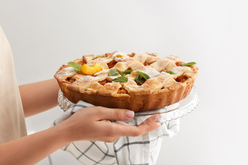 Woman with tasty peach pie on light background