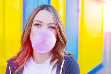 Portrait of playful blonde smiling woman blowing bubble with chewing gum on a bright colorful...