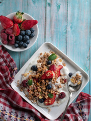 breakfast granola yogurt, strawberry, blueberries, raspberries on a white plate. on a blue table board with a towel