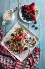 breakfast granola yogurt, strawberry, blueberries, raspberries on a white plate. on a blue table board with a towel