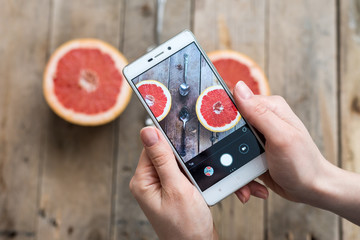close-up of fruit photo. The hand holding the phone and taking pictures of red ripe grapefruit with...