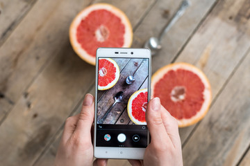 close-up of fruit photo. Girl's hands holding phone and taking pictures of red grapefruit with...