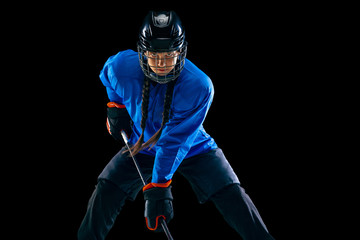 Young female hockey player with the stick isolated on black background. Sportswoman in action...