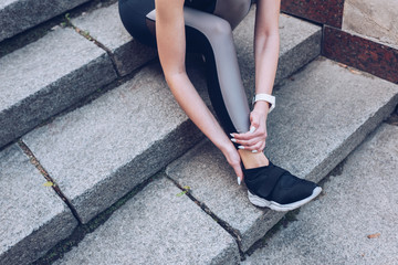 cropped shot of sportswoman sitting on stairs and touching injured leg