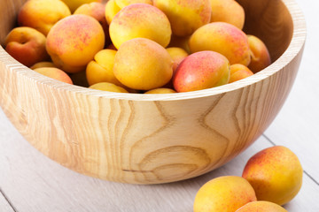 ripe organic apricots fruits in ash tree wooden bowl on a white wooden background