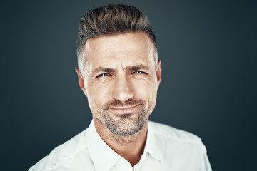 Cheerful and handsome. Handsome young man smiling and looking at camera while standing against grey background