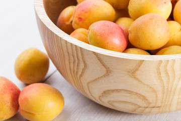 Naklejka na ściany i meble ripe organic apricots fruits in ash tree wooden bowl on a white wooden background
