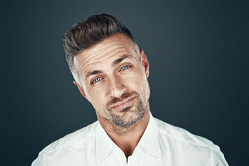 Obraz premium Uncertainty. Handsome young man looking at camera while standing against grey background