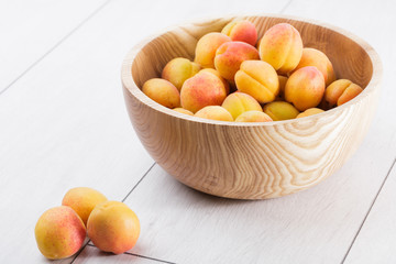 ripe organic apricots fruits in ash tree wooden bowl on a white wooden background
