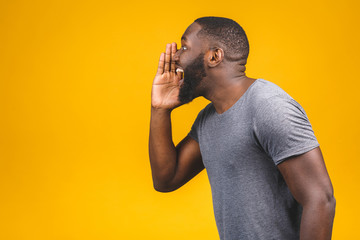 Side view portrait of a young african american man screaming out loud with hand at his mouth isolated on the yellow background. - Powered by Adobe