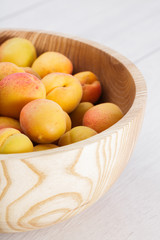 ripe organic apricots fruits in ash tree wooden bowl on a white wooden background