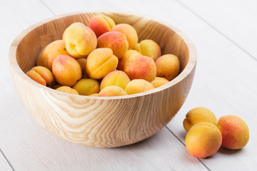 ripe organic apricots fruits in ash tree wooden bowl on a white wooden background