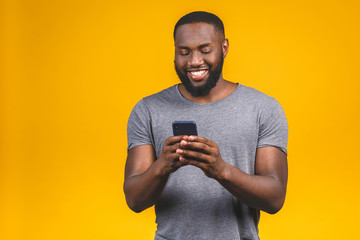 Portrait of handsome excited cheerful joyful delightful curious guy wearing casual sending and getting messages to his lover isolated against yellow background. Using phone.