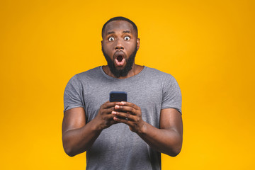Great news! Portrait of handsome excited cheerful joyful delightful curious guy wearing casual sending and getting messages to his lover isolated against yellow background. Using phone.