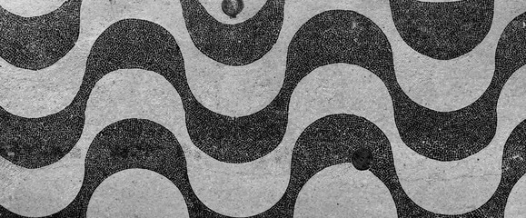 Schwarz-Weiß-Darstellung des leeren Bürgersteig-Boulevard-Wellenmusters von Kopfsteinpflaster des Copacabana-Strandes bei Sonnenaufgang am frühen Morgen in Rio de Janeiro. Nahaufnahme mit Textur des echten Straßengehwegs.