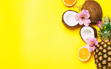 Tropic fruits and flowers: coconut, pineapple, and orange on yellow background. Top view, flat lay, copyspace for text.