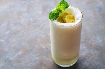 Banana Smoothie on a dark grey table and a piece of banana slide in a glass