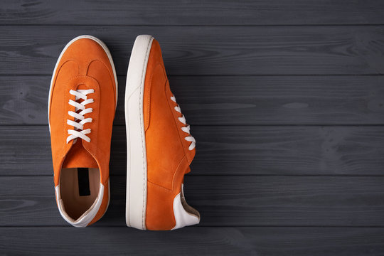 Top view of casual orange suede sneakers on grey wooden planks