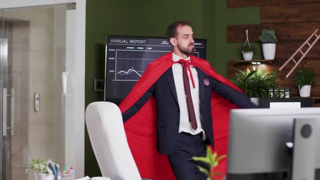 Slow motion shot of businessman wearing a red cape walking silly in the office. Conceptual footage