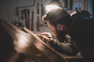 Young luthier working in his workshop, building a double bass