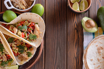 Cooking burrito with filling. A burrito flat cake filled with a variety of fresh vegetables and pieces of chicken meat on a wooden board next to the lime, top view
