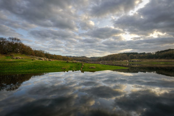 Fototapeta premium Spectacular cloudscape over green fields at the edge of a calm waters