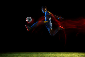 Young african-american male football or soccer player in sportwear and boots kicking ball for the...