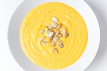 Pumpkin soup with seeds. White plate on white background. Food photography