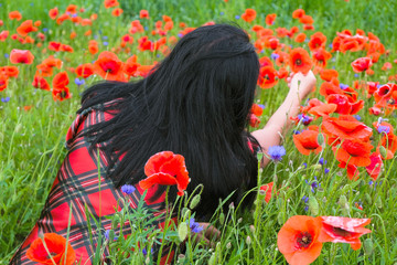 Naklejka premium A woman with black hair in a red shirt sat down in a field with flaming poppies. The woman feels relaxed.