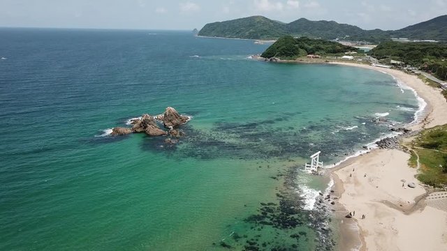 aerial footage of blue ocean, the twin rocks and the white torii gate on the water at the coast of sakurai futamigaura beach, itoshima fukuoka japan v02